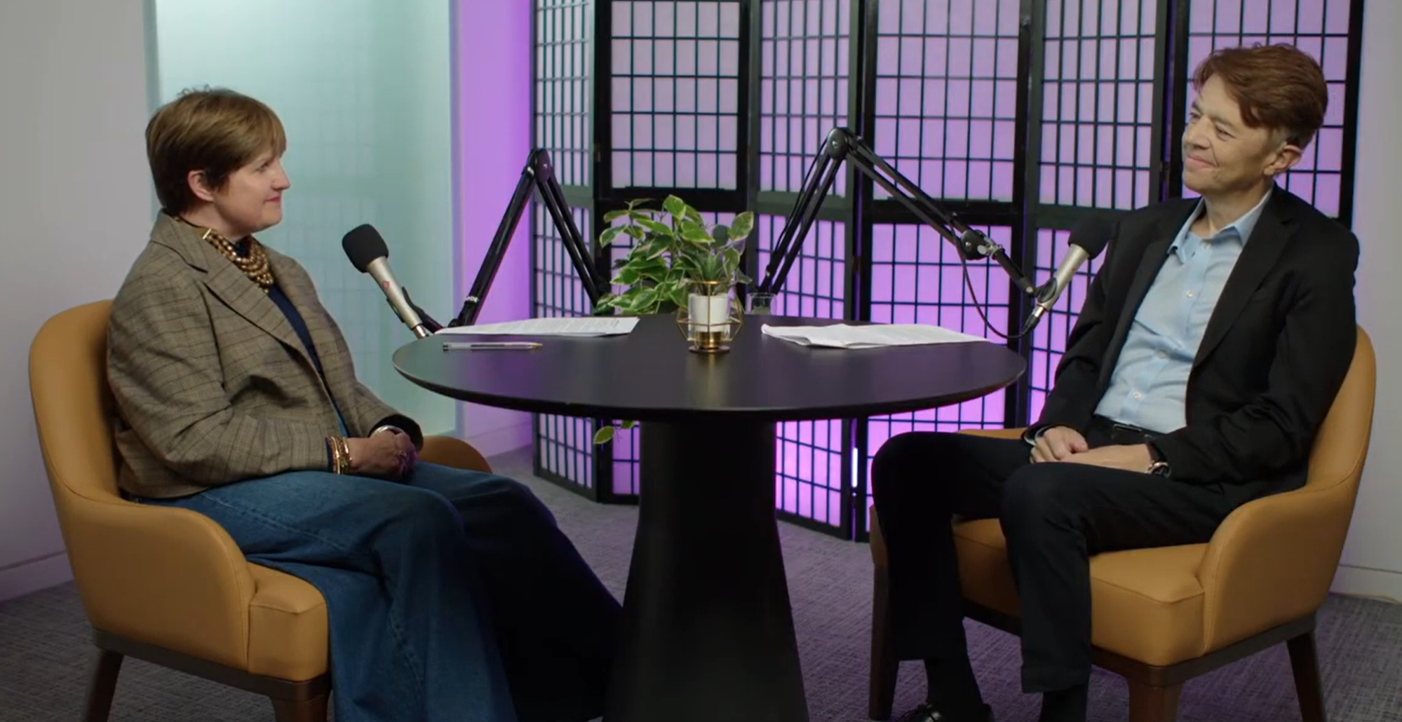 Image of Kate and Matt in the Confident Conversations podcast studio at a table with individual microphones. They smile at each other during their conversation