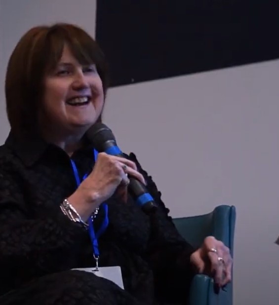 Image of Kate at the NHS Disability Summit, laughing on stage during her presentation, mic in hand